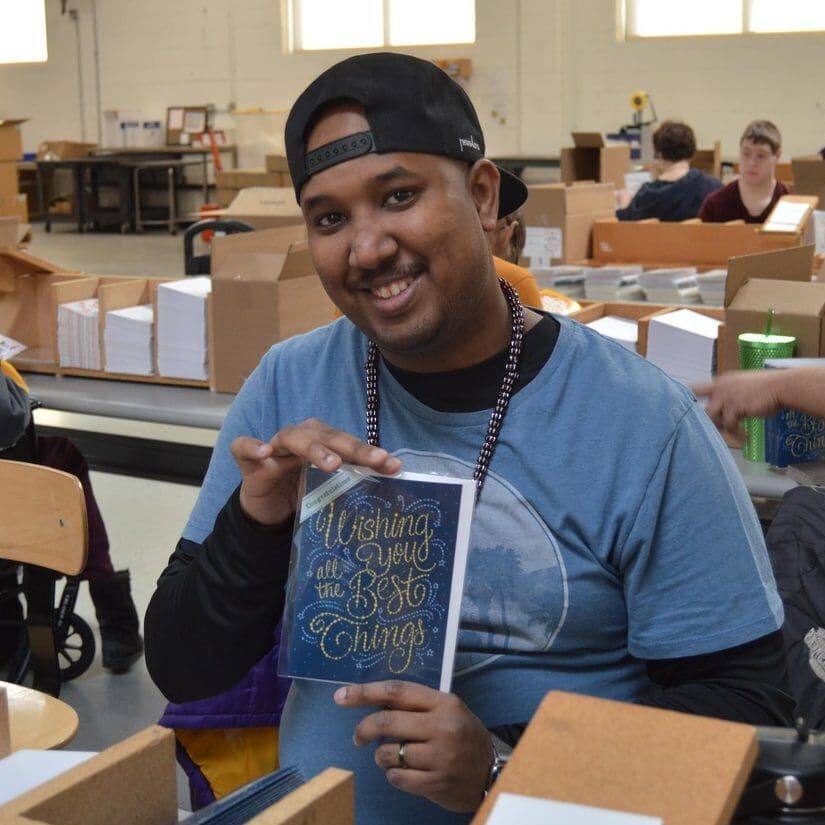 An individual confidently holds up a greeting card at their work station.